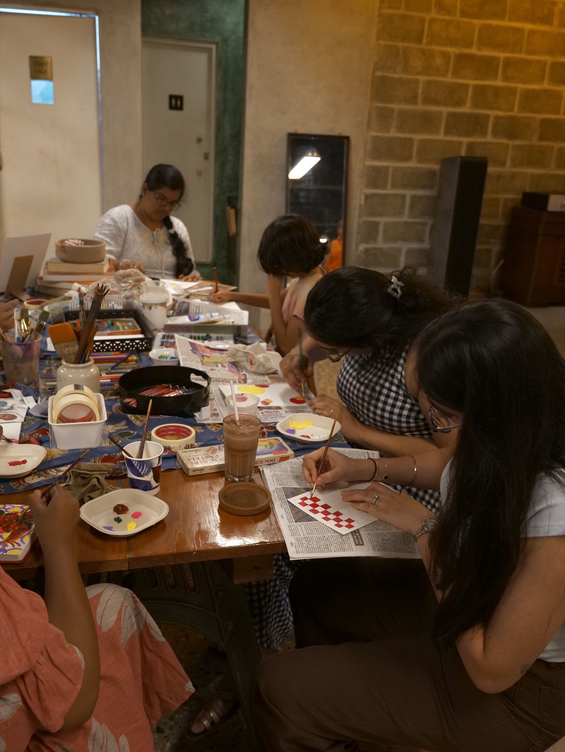 Participants paint small geometric designs at a shared workshop table.