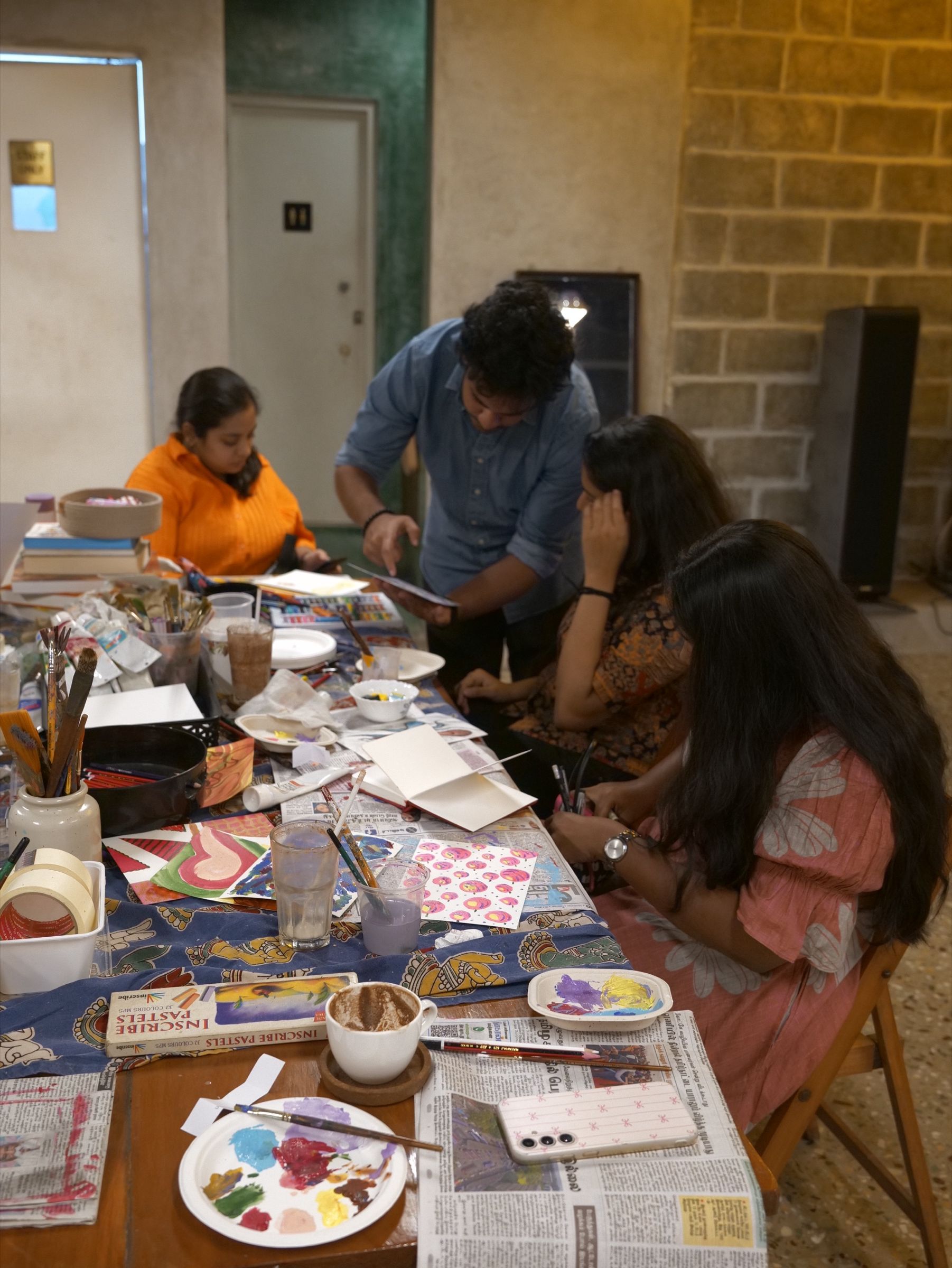 Pastels, drawings and coffee cups arranged across a workshop table.