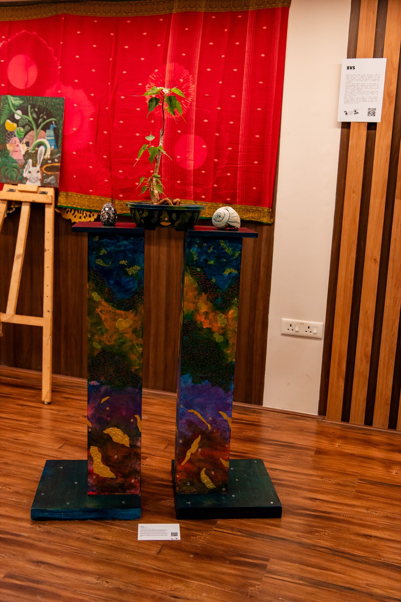 An installation with a potted plant and two small sculptural forms raised on painted plinths.