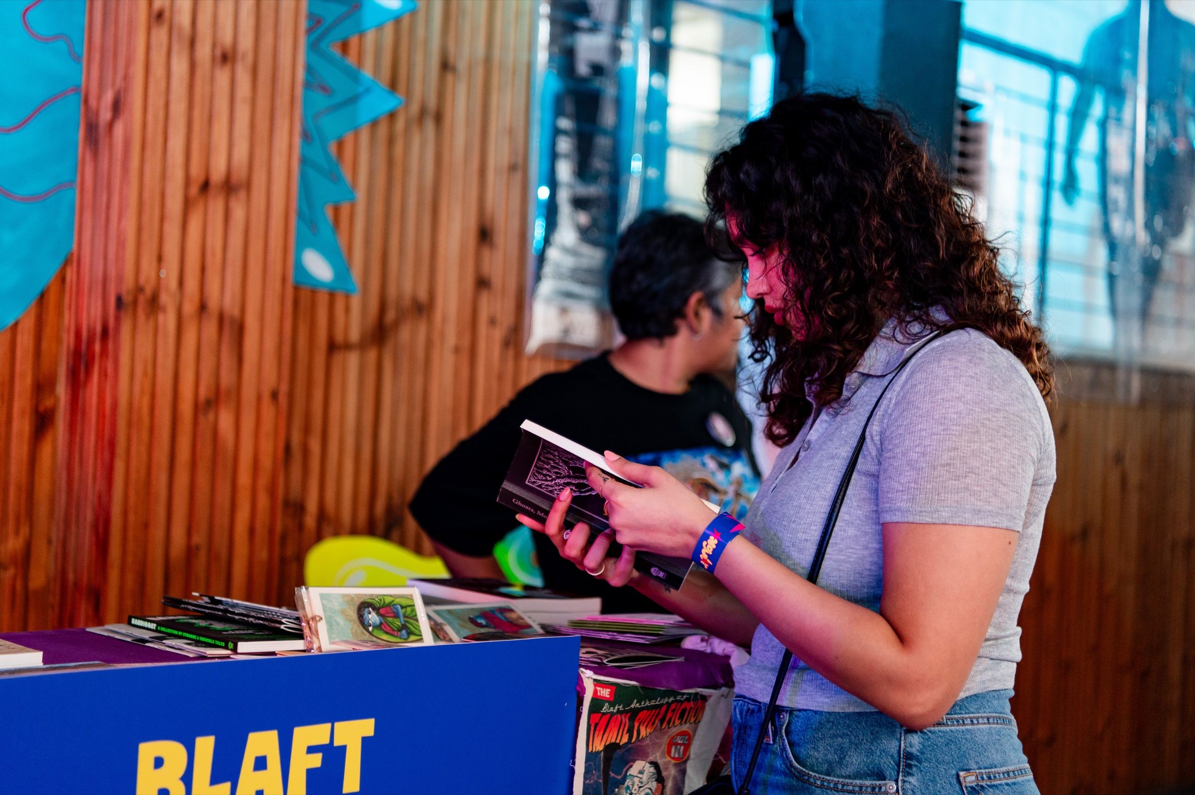 A visitor reads a small book at the Blaft Publications stall, surrounded by illustrated books and prints.