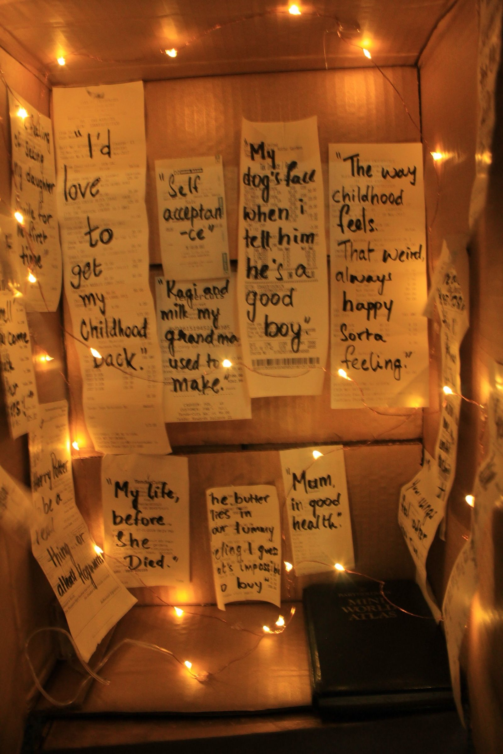 Handwritten memories and reflections displayed under warm lights inside a cardboard chamber.