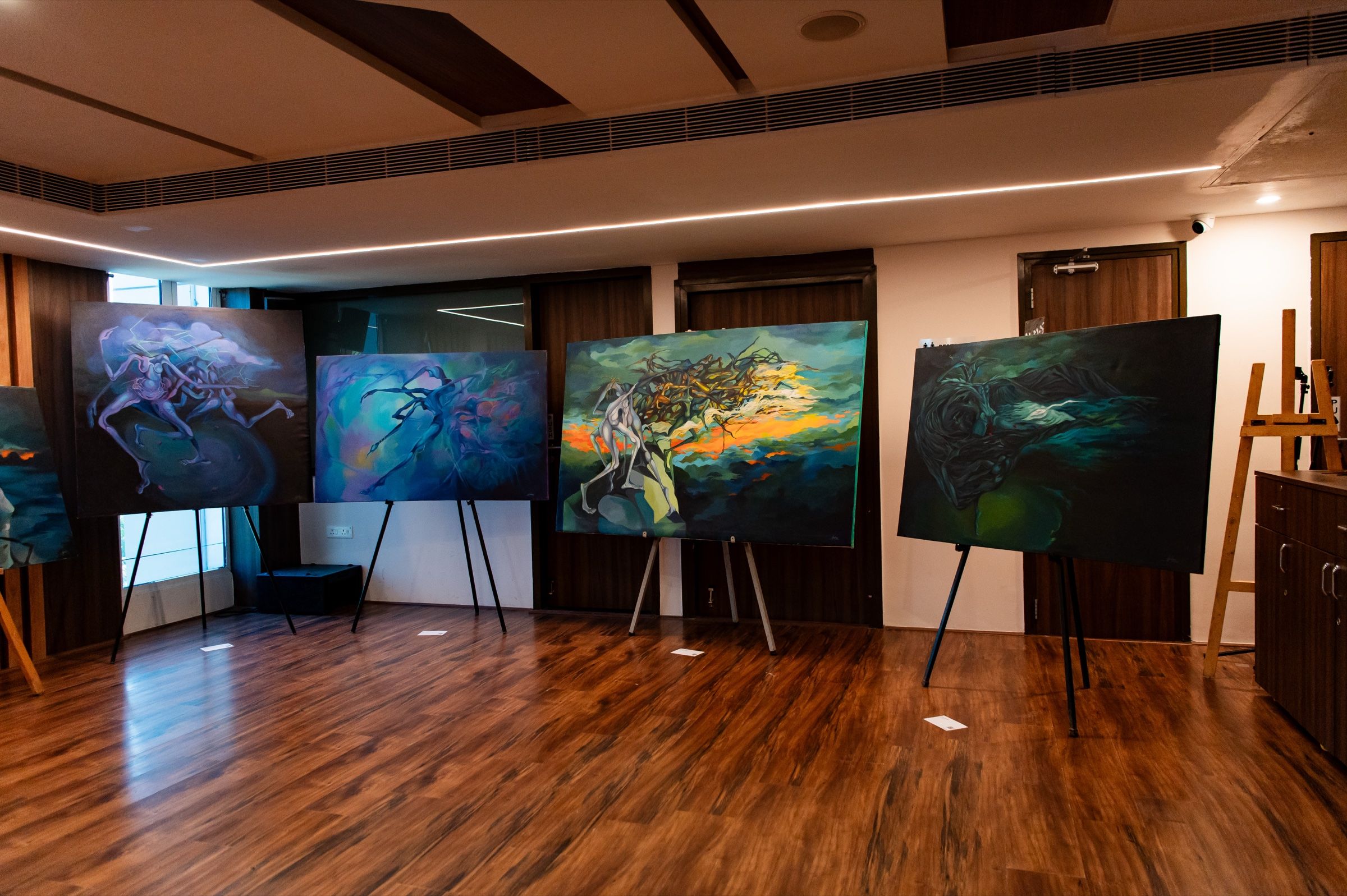 Five large blue-green figurative paintings displayed on easels across the gallery.