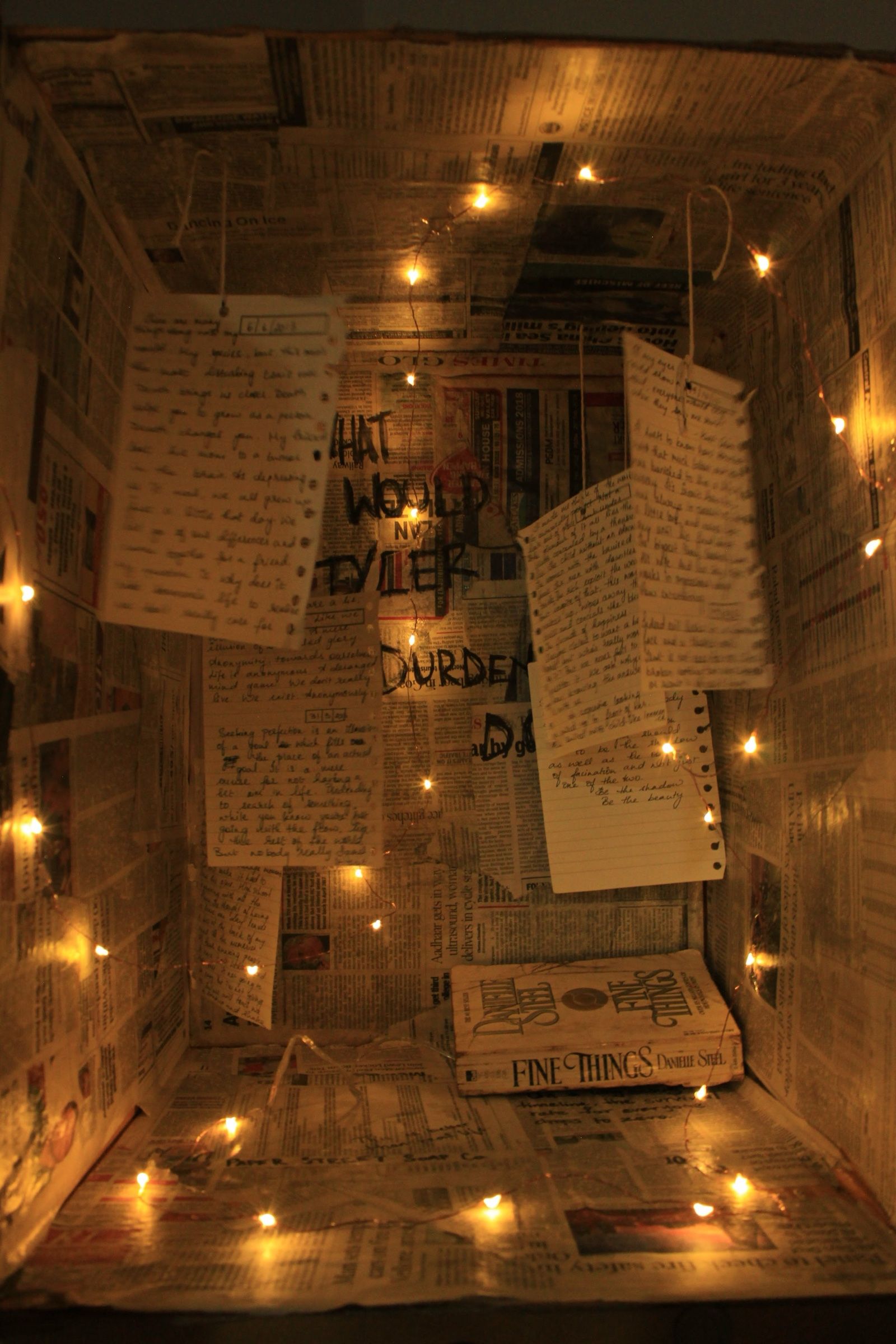 Family photographs, handwritten captions and a single shoe inside an illuminated cardboard shrine.