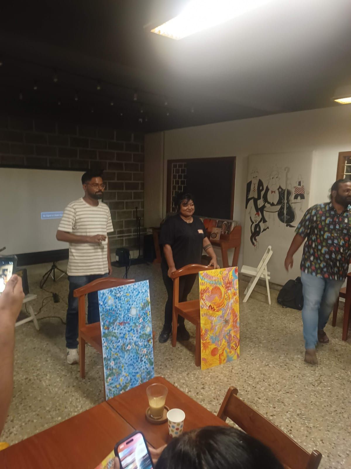 Rhea standing with two colourful live paintings at the Focus Group Radio Exotica listening session.