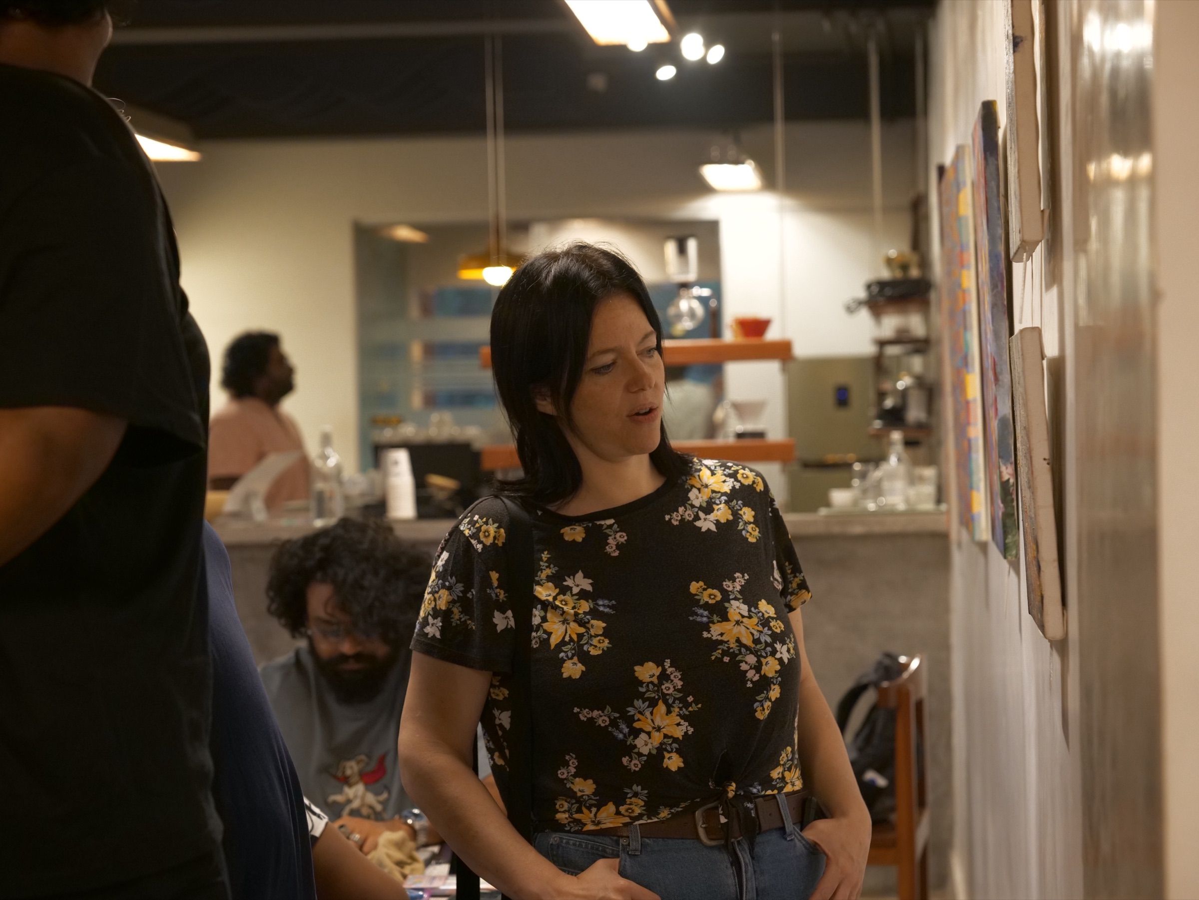 Visitors talk while looking at paintings displayed along the exhibition wall.